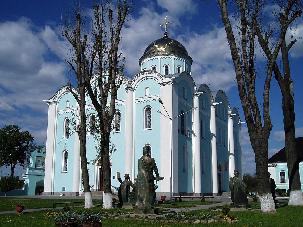 Hellblaue Mariä-Entschlafens-Kathedrale in Wolodymyr mit Bronzeskulpturen im Vordergrund